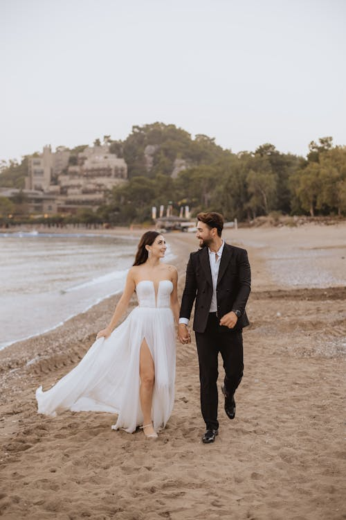 Newlyweds walking hand-in-hand along the shoreline at a beach wedding